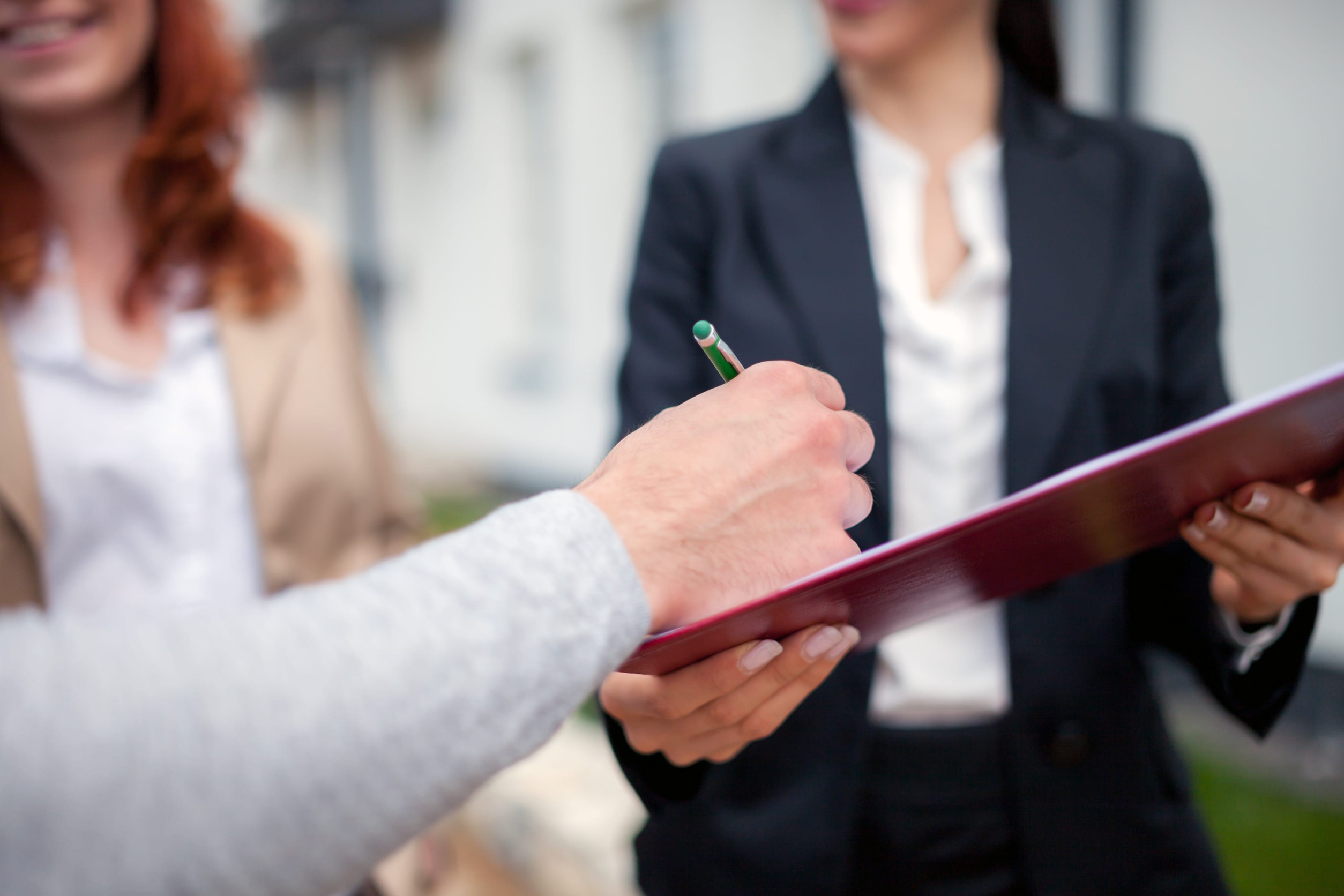 A homebuyer signs purchase documents while a real estate agent holds the paperwork, representing a confident and well-prepared offer during the home buying process.