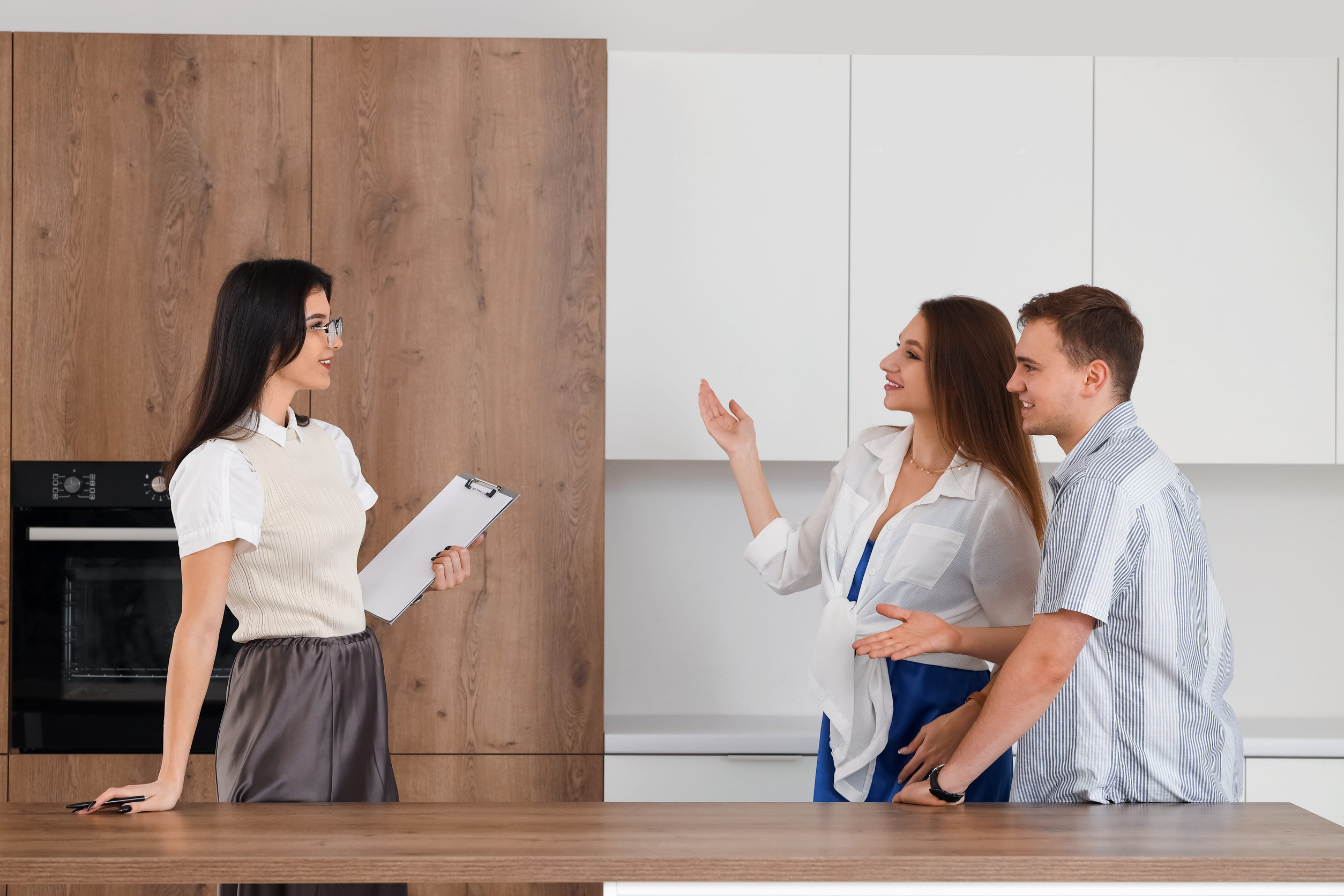 A real estate agent speaks with a young couple inside a modern home during a property tour. The buyers smile and ask questions while discussing the home's features, highlighting a relaxed and informative home-buying experience.